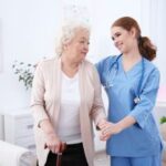 Smiling nurse assisting elderly woman with cane